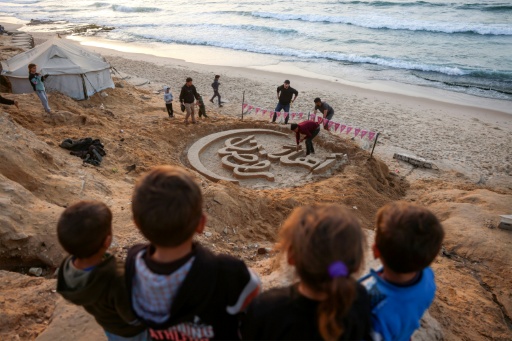 Des enfants regardent une sculpture de sable proclamant Bienvenue au ramadan, le 17 février 2026 sur une plage de Gaza