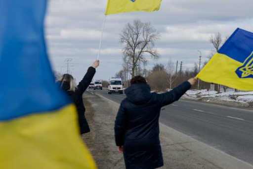 Des personnes agitent des drapeaux sur le bord d'une route à l'approche d'un convoi de soldats libérés par les Russes après un échange de prisonniers, le 6 mars 2026 dans un lieu non précisé dans le nord de l'Ukraine