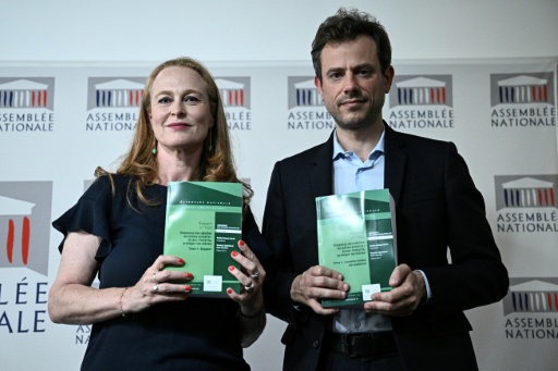 Une femme et un homme posent côte à côte en tenant des rapports verts, devant un fond Assemblée nationale