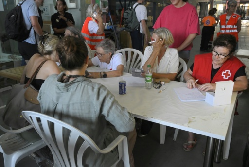 Des personnes évacuées assises autour d'une table avec des bénévoles de la Croix-Rouge dans un gymnase