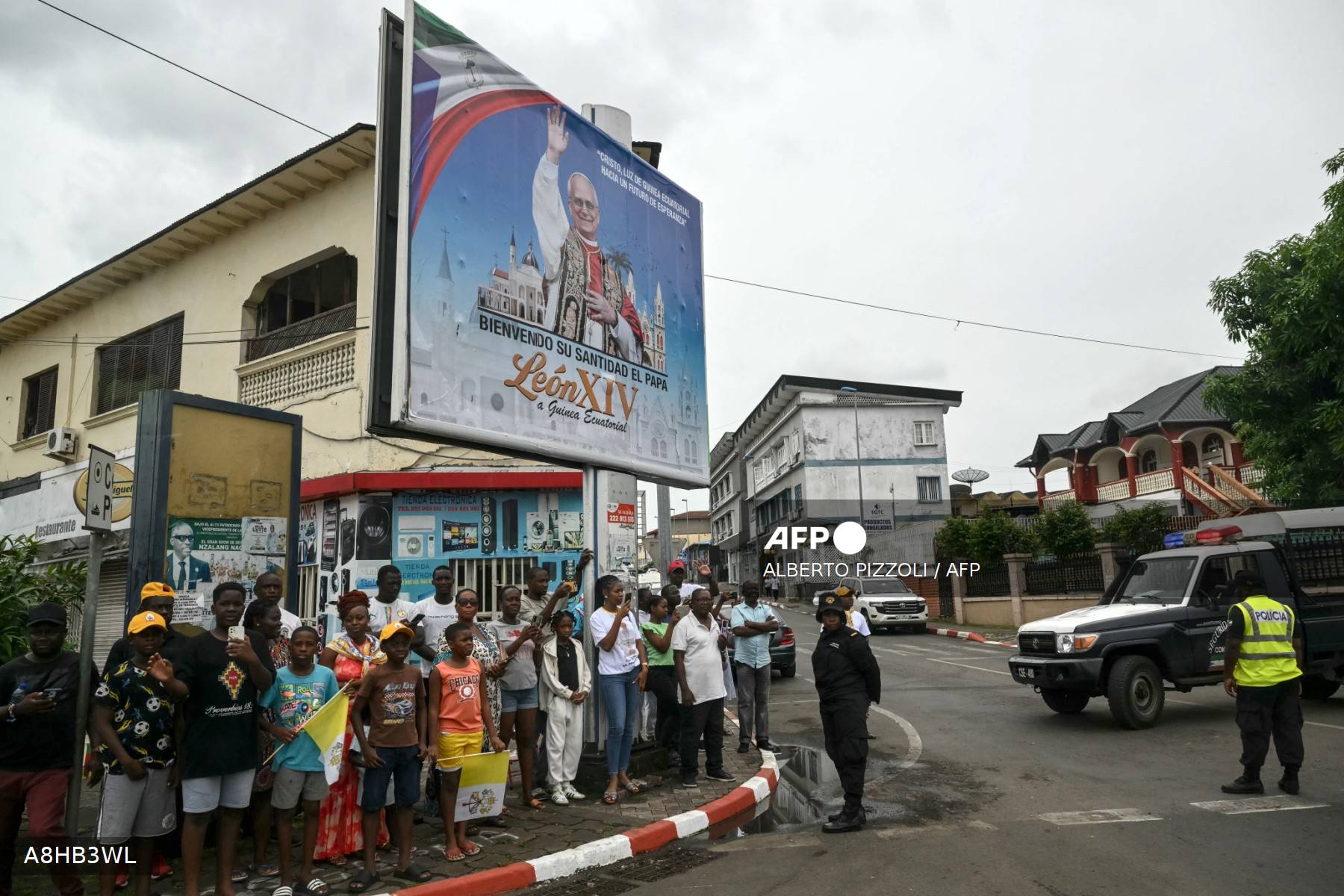 Panneau officiel «&nbsp;Bienvenido Su Santidad El Papa León XIV&nbsp;» à Malabo, fidèles et voiture de police le 21 avril 2026