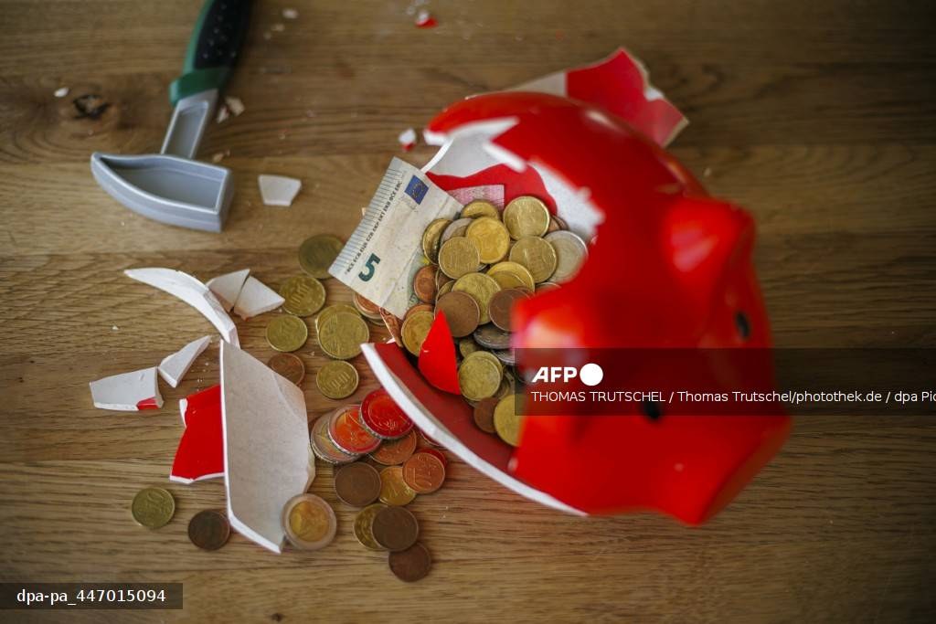 Une tirelire rouge brisée au marteau, pièces et billet répandus sur une table en bois