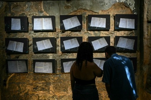 Des visiteurs devant des documents d’archives exposés sur un mur criblé d’impacts à Beit Beirut