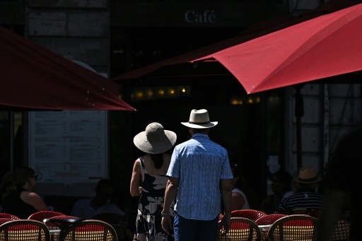 Un couple marche en plein soleil devant la terrasse d'un café