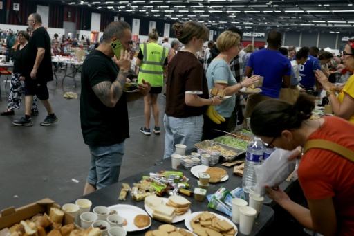 Des personnes évacuées font la queue devant des tables de petit-déjeuner dans un grand hall