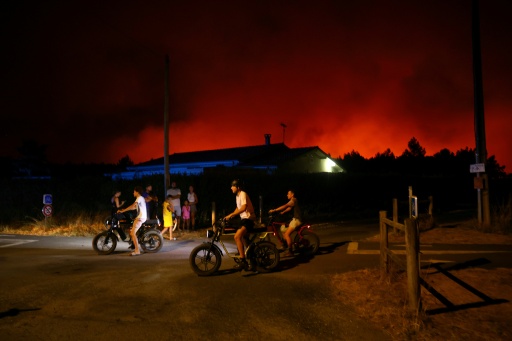 Des habitants à vélo devant un ciel nocturne rougi par l'incendie