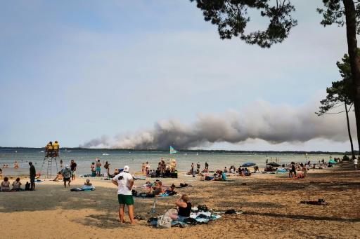 Des vacanciers assis sur la plage, un épais nuage de fumée dans le ciel