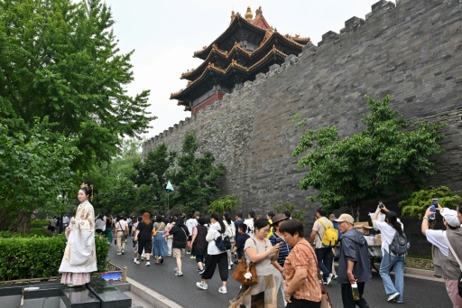 Une femme en tenue traditionnelle pose devant la Cité interdite à Pékin, au milieu des touristes