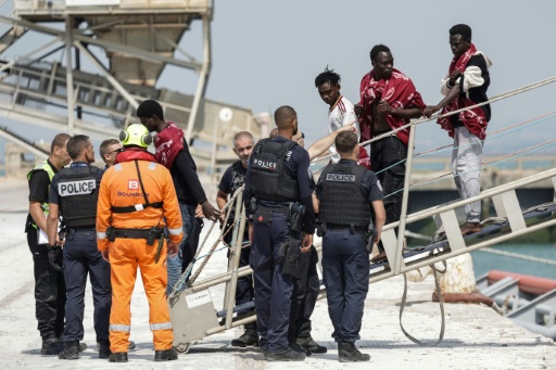 Des personnes secourues en mer descendent d’un navire sous la surveillance de policiers, au port de Boulogne-sur-Mer