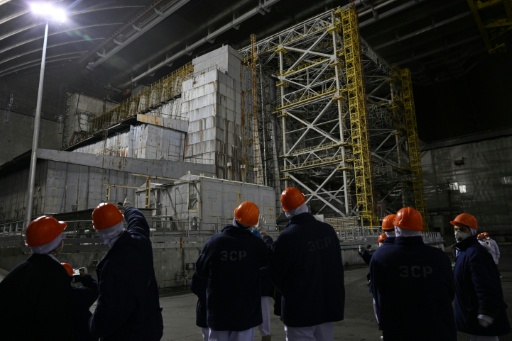 Des représentants de Greenpeace et des médias sous la nouvelle enceinte de confinement de Tchernobyl, devant le sarcophage du réacteur 4, le 9 avril 2026